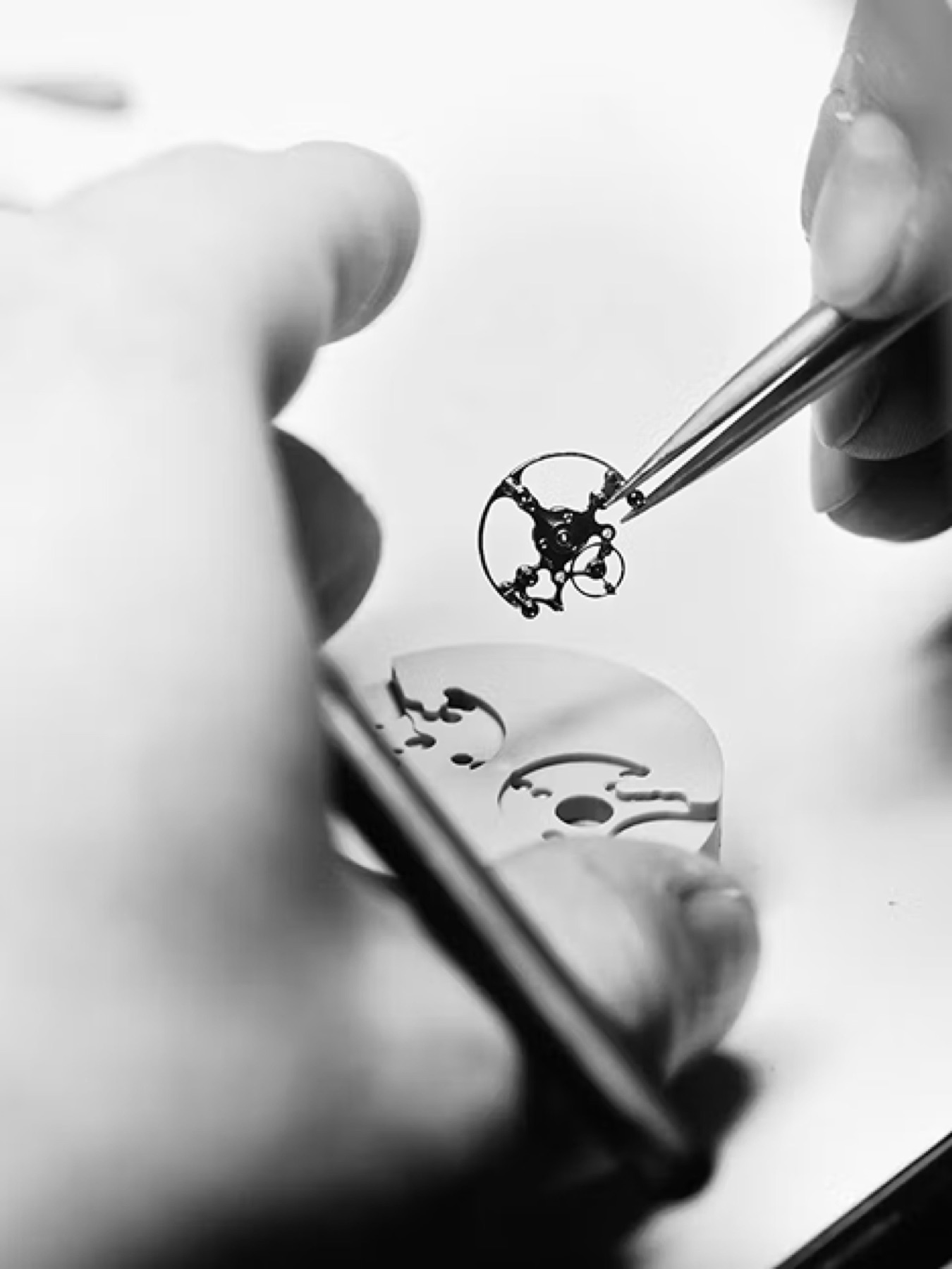 A watchmaker placing a balance wheel with tweezers
