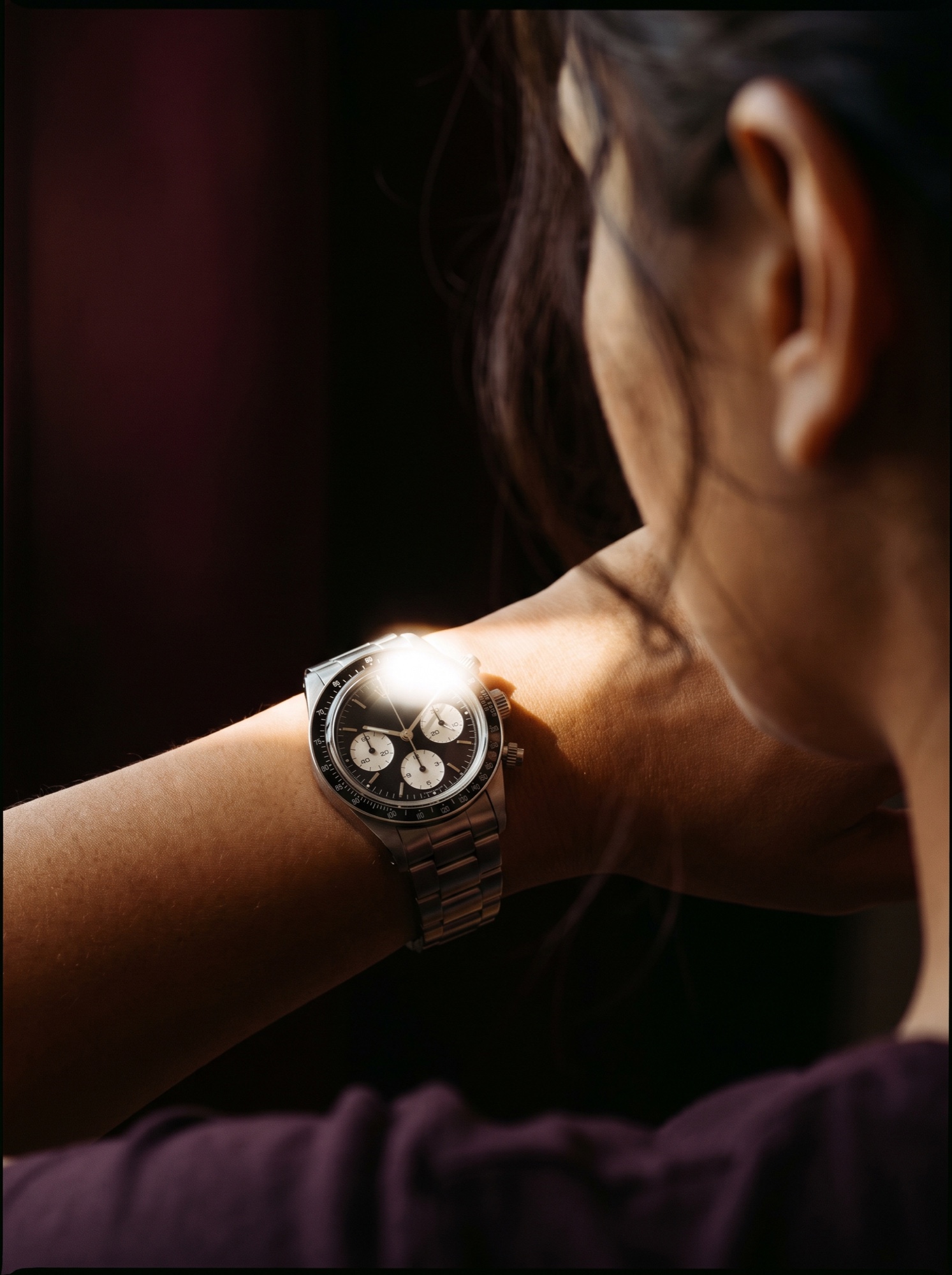 A steel chronograph worn on a raised wrist, seen past the shoulder