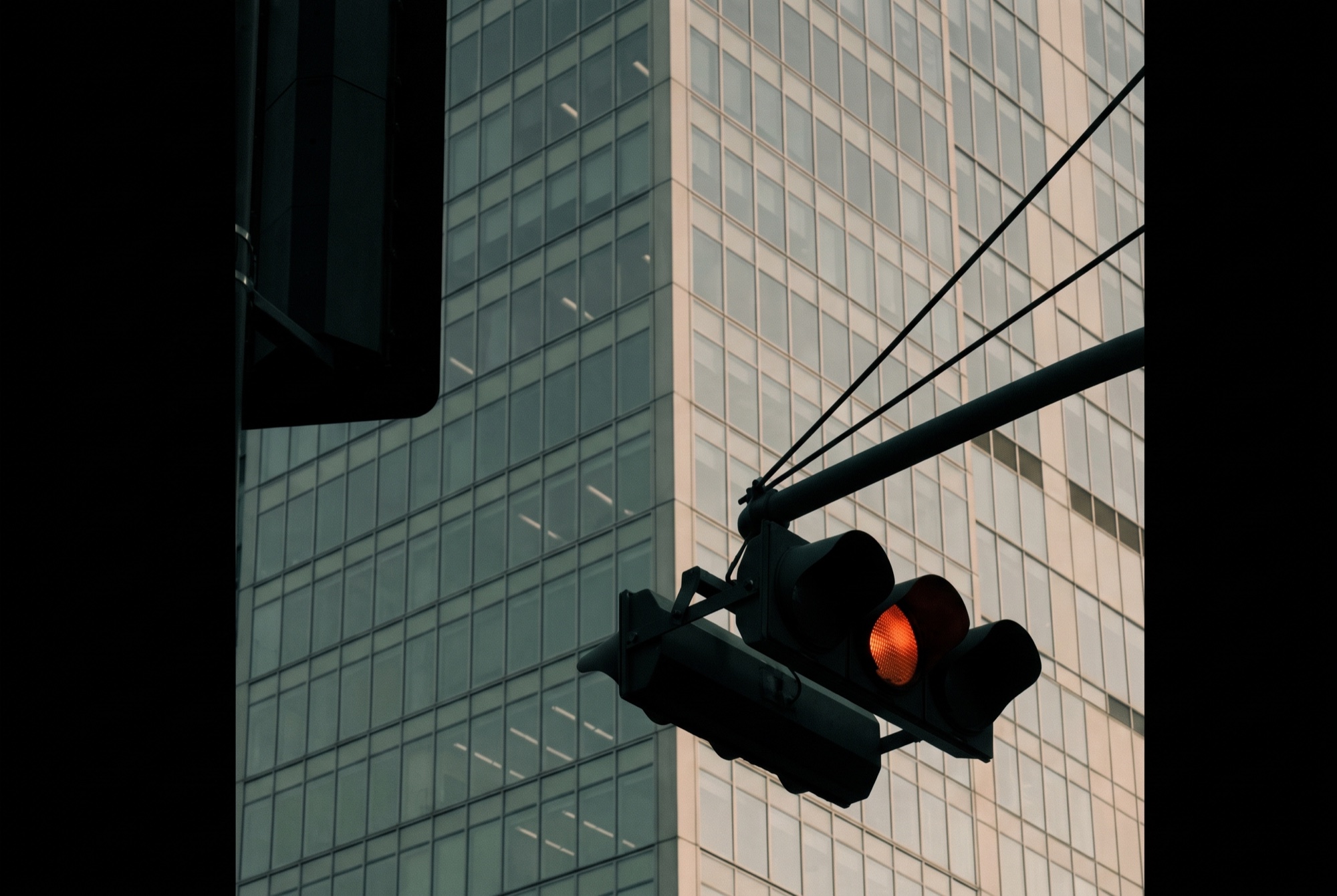 A traffic signal in silhouette against a glass tower